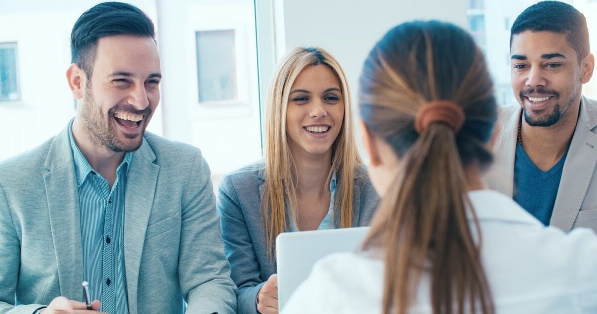 Tres personas entrevistando a una mujer de espaldas en una entrevista para selección de personal por parte de una consultora de RRHH