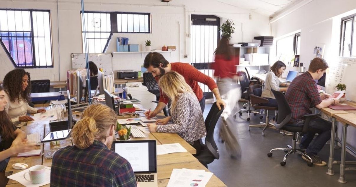 Oficina de trabajo con mesas grandes y empleados separados tras volver a trabajar después de la pandemia